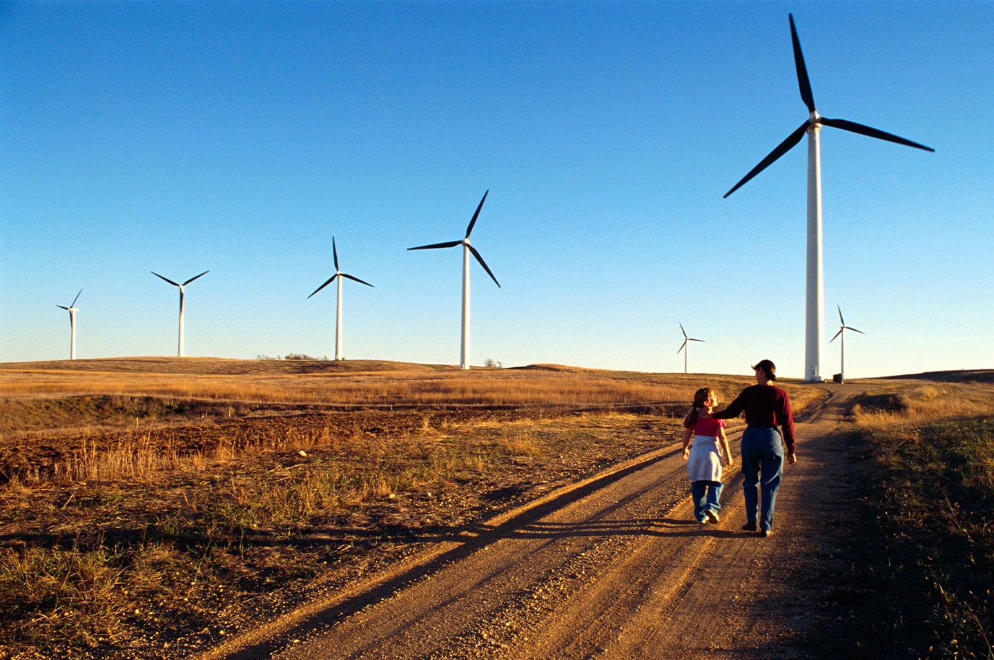 Mother and daughter walking toward wind turbines on a hill