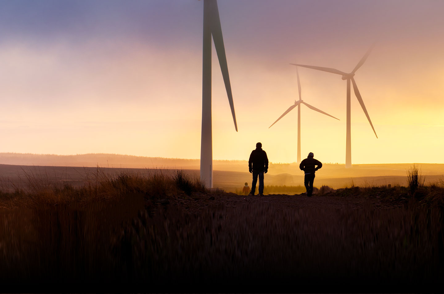 People at the base of wind turbines at sunrise